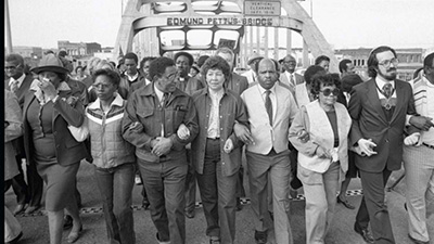A black and white photo of people gathered at the Edmund Pettus Bridge.