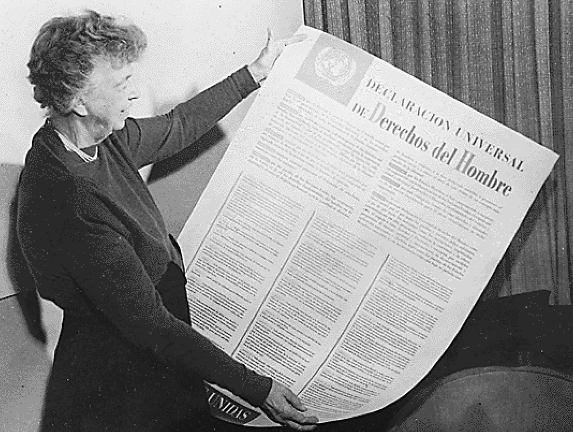 A photograph of a woman holding up a very large document, the Spanish Language translation of the Universal Declaration of Human Rights.