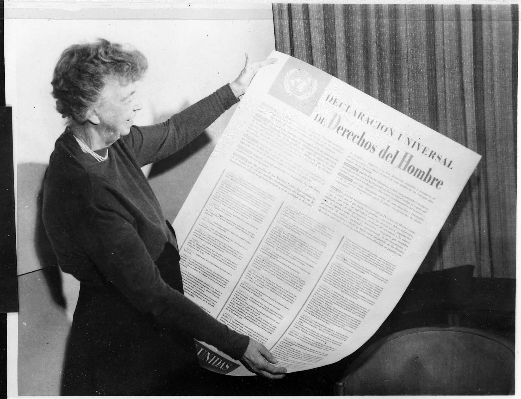 Photo of Eleanor Roosevelt holding a large sheet of paper that contains the Spanish version of the United Nations Universal Declaration of Human Rights.