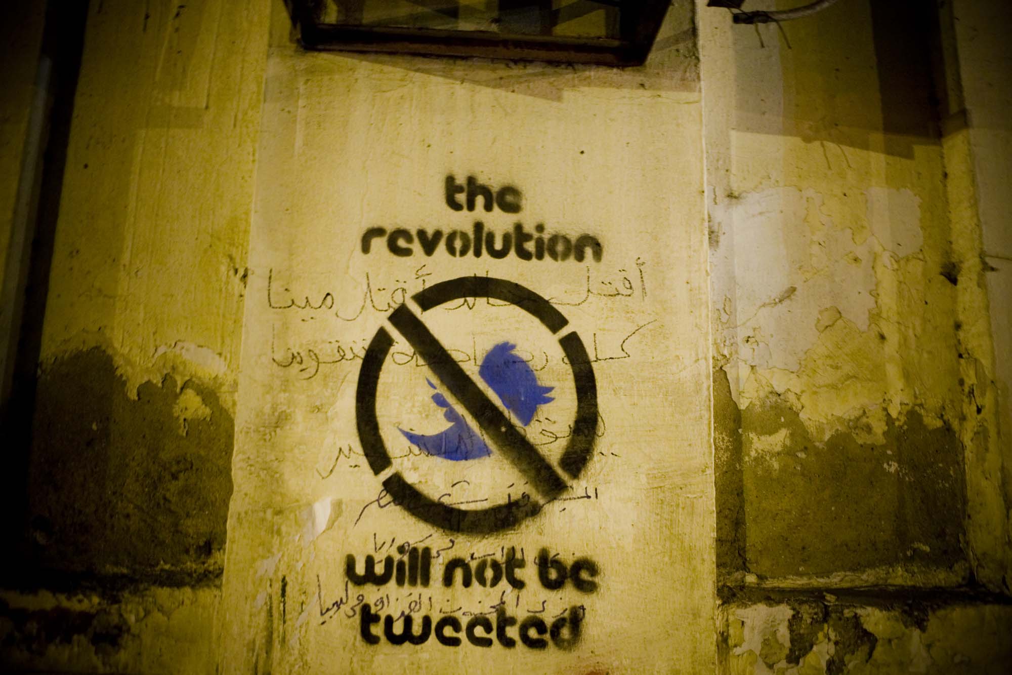 Photo of a graffitied wall with a crossed-out Twitter logo and the words, “the revolution will not be tweeted” written on it.
