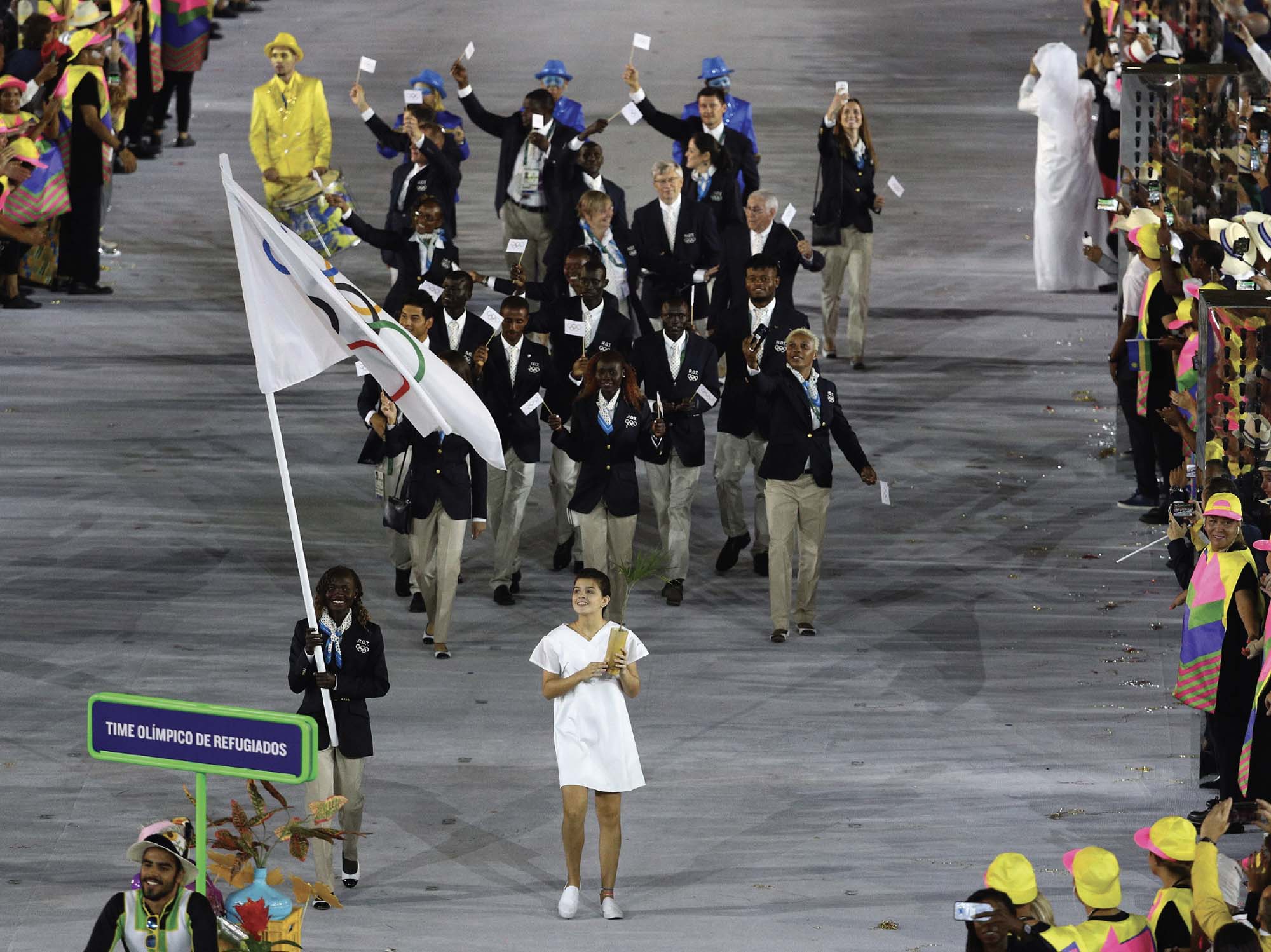 Photo of the Refugee Olympic Team during the Opening Ceremony of the 2016 Olympics. The refugees wave flags bearing the Olympic rings.
