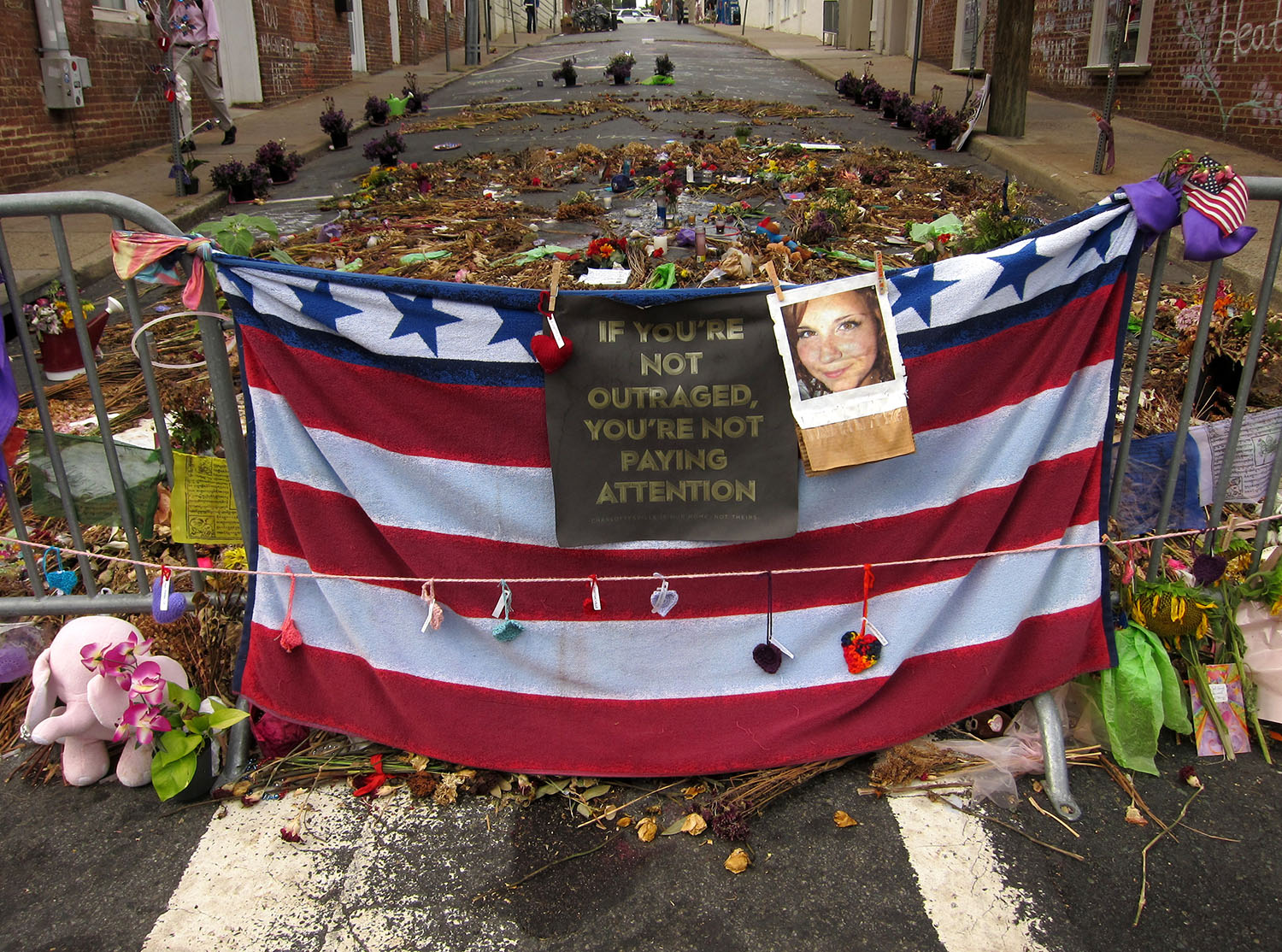 A street memorial with American flag towel tied between two steel barriers. Flowers, mementos are scattered in honour of the victim.