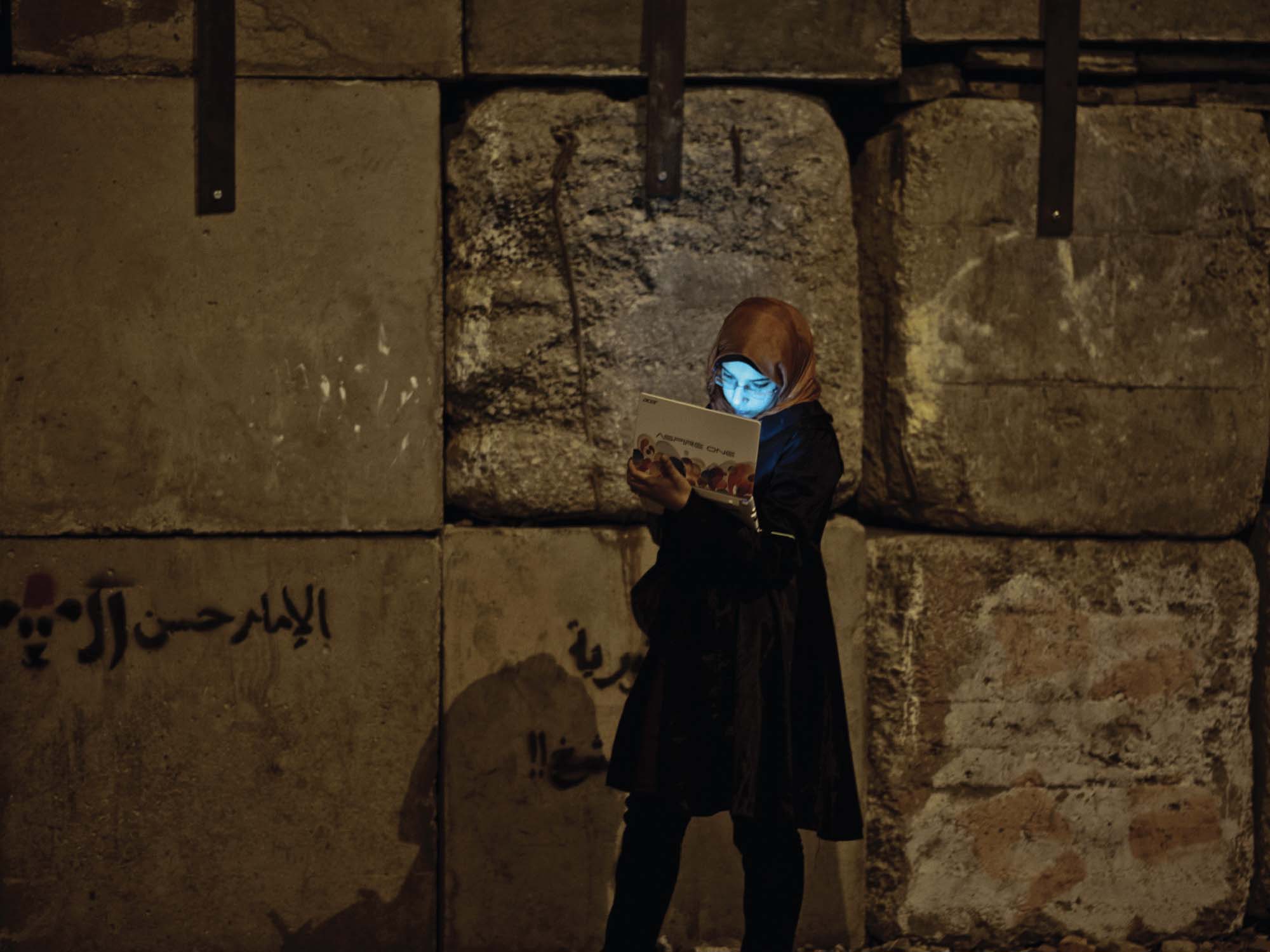 Photo of a young woman in a hijab using her laptop outside the presidential palace walls of the Morsi government.