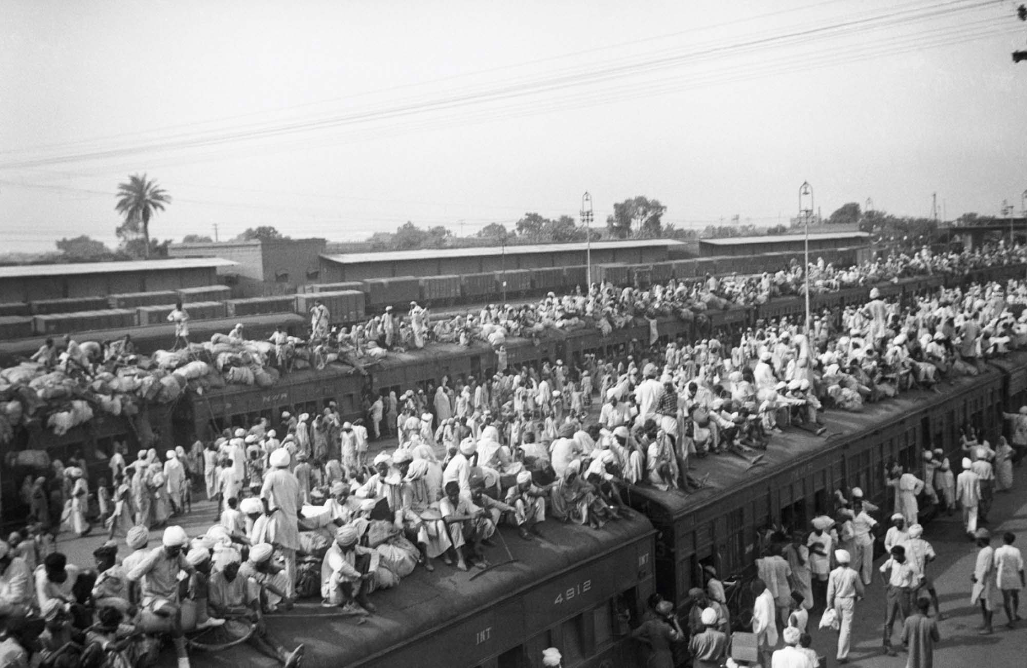 Black and white photograph of crowds of people outside and on top of trains at a station.